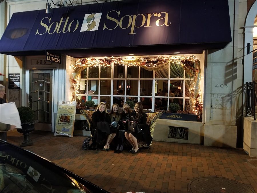 Guests outside Sotto Sopra beneath its blue awning and illuminated windows
