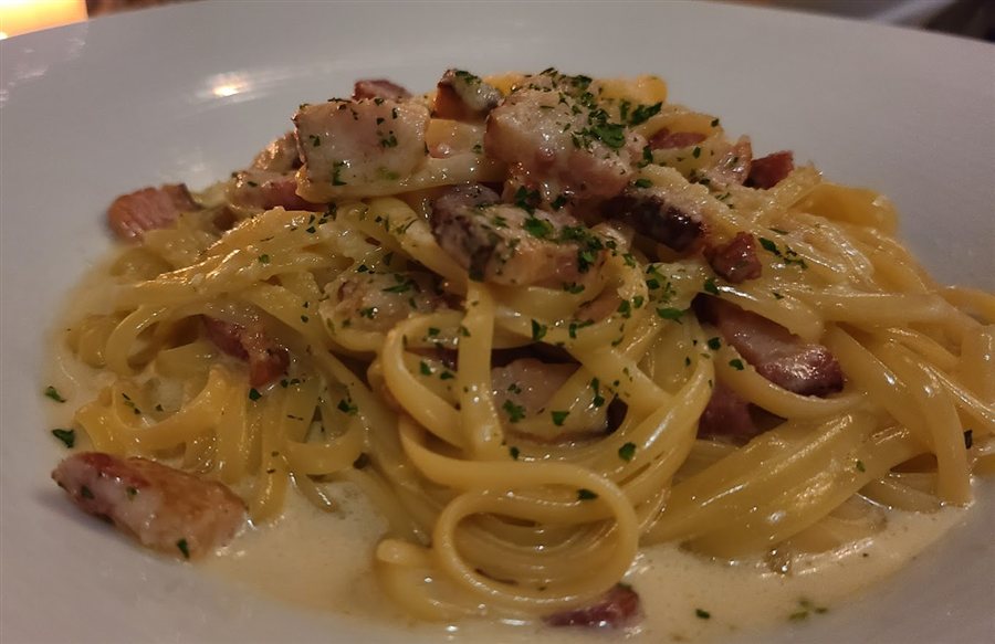 Creamy long pasta with herbs and diced meat on a white plate