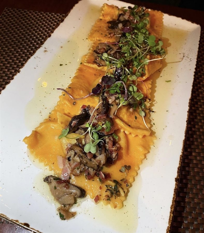 Filled pasta topped with mushrooms and greens on a rectangular plate