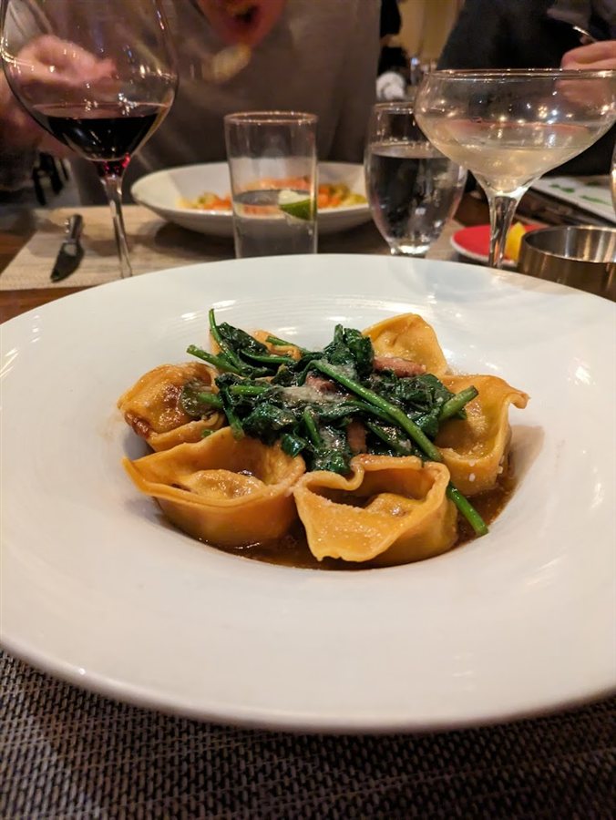 Filled pasta with greens at a table set with wine glasses