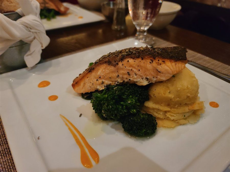 Salmon served with greens and a golden side on a white plate