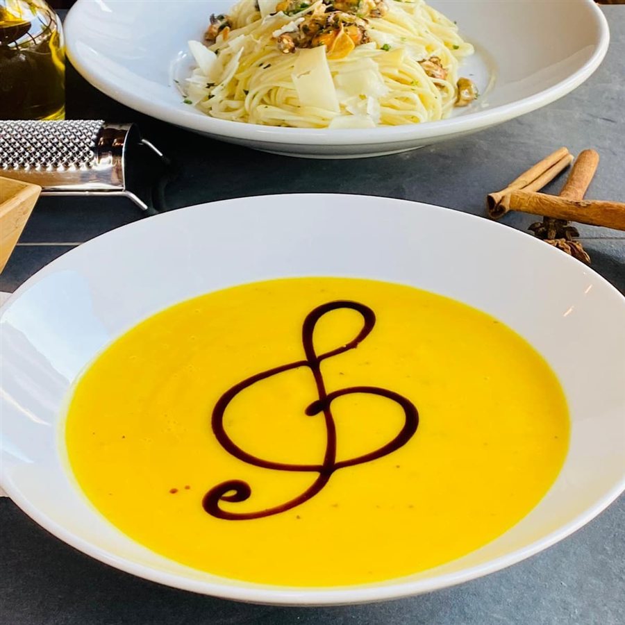 Golden soup with a musical-note garnish, with pasta in the background