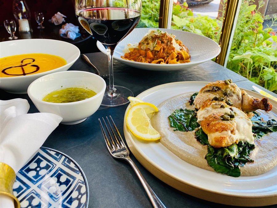 Roasted chicken, pasta, soup and red wine beside a bright restaurant window